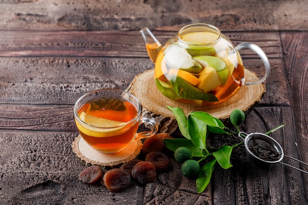 Fruta infundida de agua en la tetera con té de albaricoques secos, madera, contenedor, limas, ángulo de visión alta sobre una superficie de baldosas de piedra