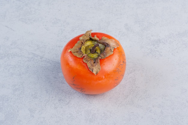 Fruta madura de caqui naranja sobre fondo gris.