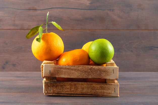 Fruta naranja mandarina y limón verde en caja de madera sobre superficie marrón