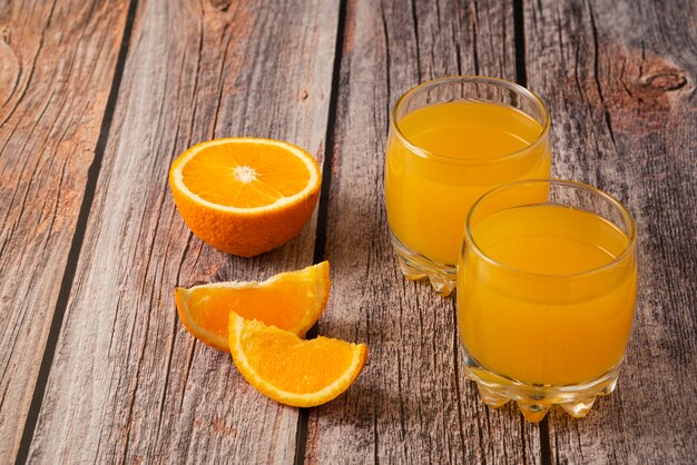 Fruta naranja con un vaso de jugo en la mesa de madera