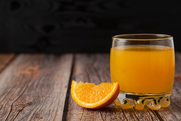 Fruta naranja con un vaso de jugo en la mesa de madera