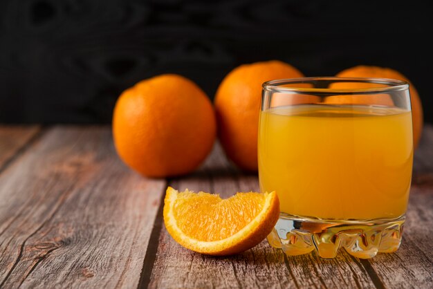 Fruta naranja con un vaso de jugo en la mesa de madera