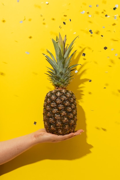 Fruta de piña sostenida a mano con confeti