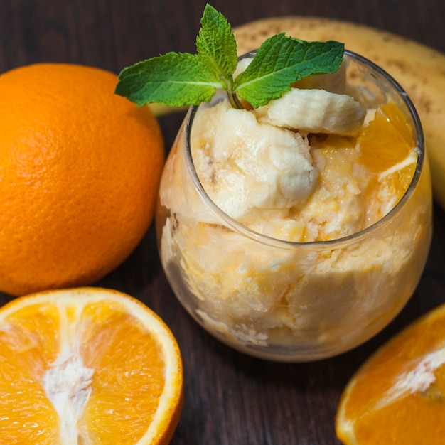 Foto gratuita fruta de plátano y naranja con menta en vaso con frutas enteras en mesa de madera