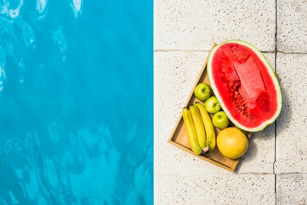 Frutas en bandeja colocadas en borde de piscina.