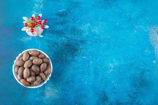 Frutas de cereza en un jarrón junto a nueces pecanas en un recipiente, sobre la mesa azul.