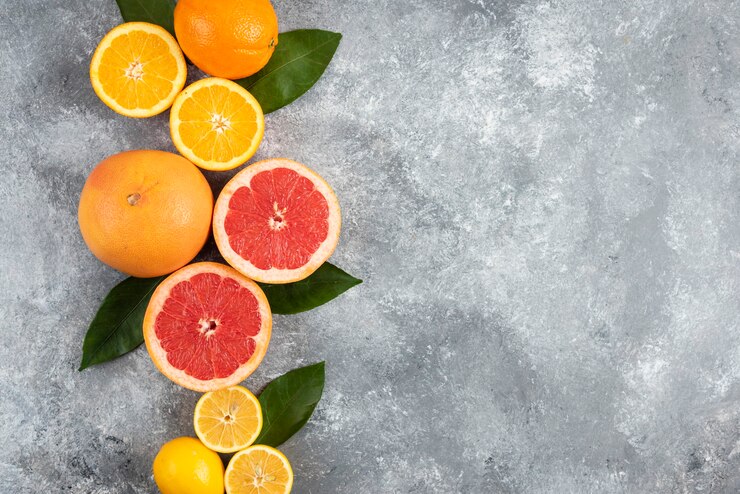 Foto gratuito frutas cítricas frescas, medio cortadas o frutas enteras sobre superficie gris.