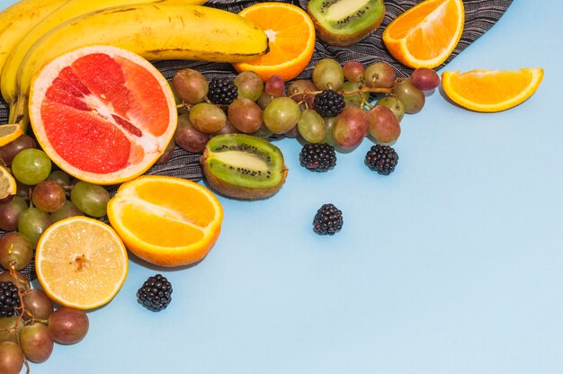 Frutas cítricas a la mitad; uvas; plátano; kiwi sobre fondo azul