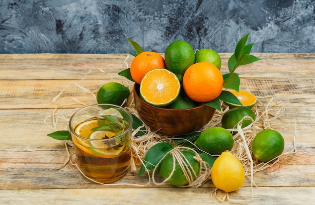 Frutas cítricas en una olla con té de hierbas sobre tablero de madera y superficie de mármol azul