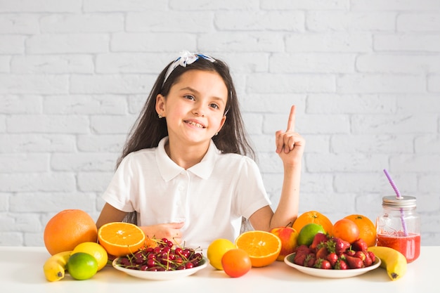 Frutas coloridas frente a una chica apuntando el dedo hacia arriba