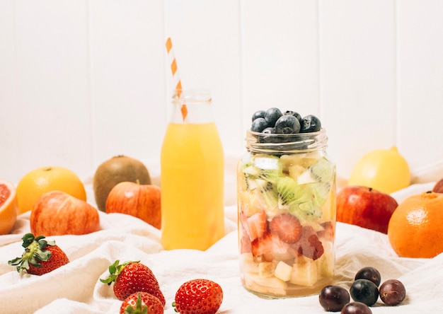 Frutas coloridas en un tarro junto a un batido de naranja.