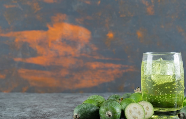 Frutas de feijoa y vaso de jugo en mesa de mármol.