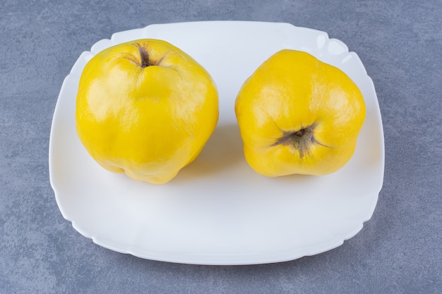 Frutas frescas de membrillo en placa sobre mesa de mármol.