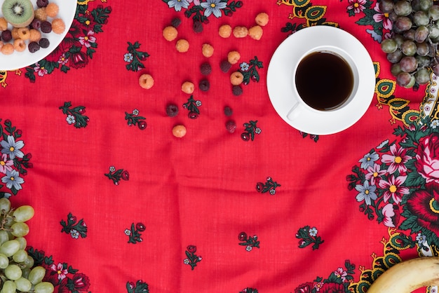 Foto gratuita frutas frescas con taza de café negro sobre mantel floral rojo