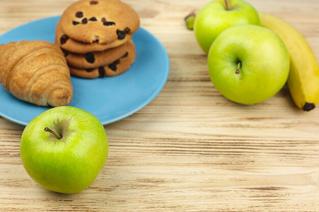 Frutas con galletas y placa de croissant en una mesa de madera