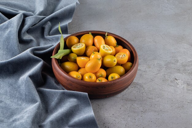 Frutas de kumquat en un recipiente sobre un trozo de tela, sobre la superficie de mármol