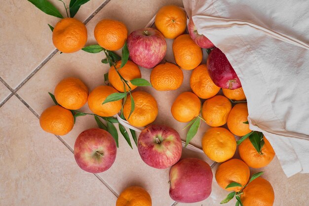 Frutas maduras coloridas en una bolsa ecológica reutilizable en un suelo de baldosas Entrega de mandarinas y manzanas Alimentos saludables vitaminas Vista desde arriba