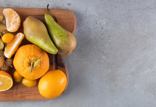 Foto gratuita frutas maduras frescas sobre una tabla de cortar de madera colocada sobre un fondo de piedra.