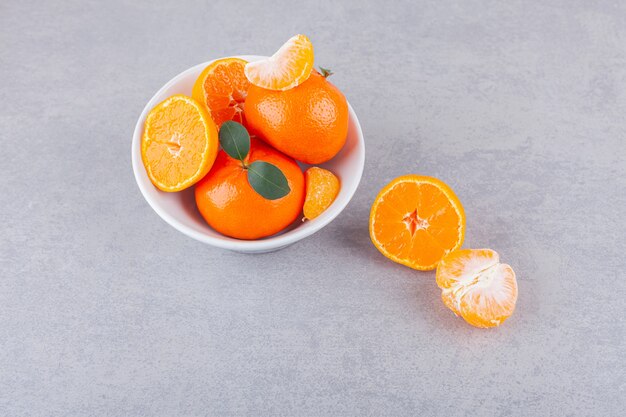 Frutas mandarina enteras y en rodajas con hojas colocadas sobre una mesa de piedra.