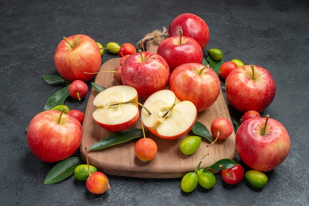 frutas manzanas y cerezas con hojas en el tablero junto a las frutas