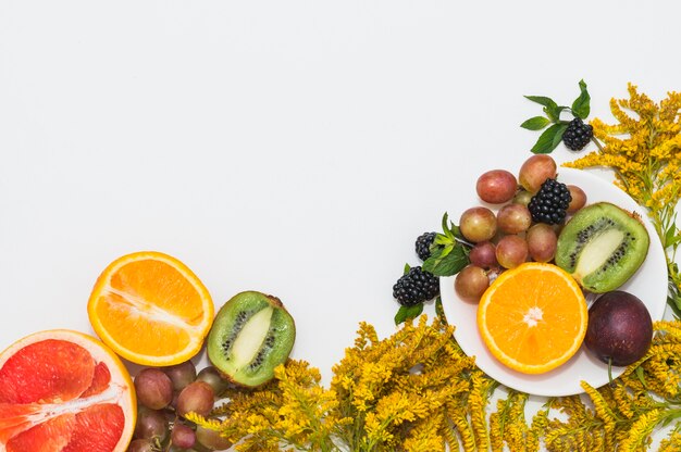 Frutas a la mitad; uvas; Moras y flores hermosas amarillas sobre fondo blanco