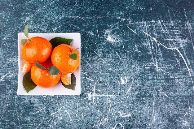 Frutas naranjas enteras con hojas verdes colocadas en un plato blanco.