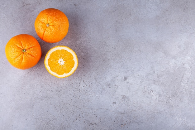 Frutas naranjas enteras y en rodajas colocadas sobre un fondo de piedra.