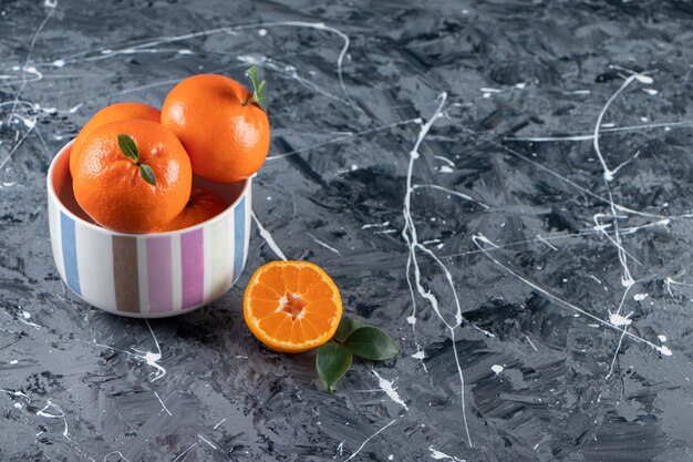 Frutas naranjas frescas en rodajas y enteras con hojas colocadas en un tazón de colores.