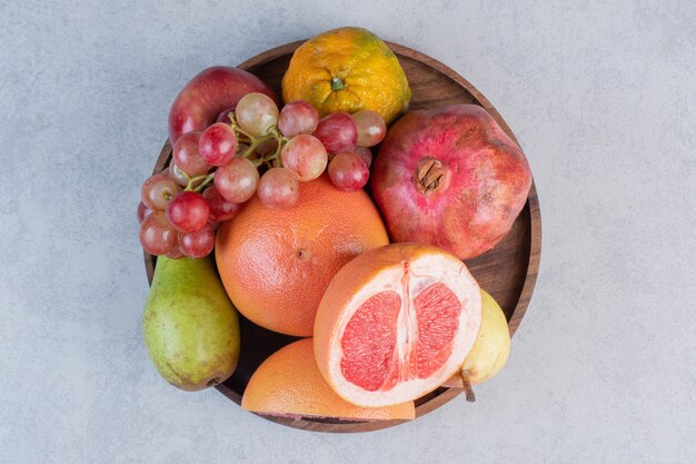 Frutas orgánicas frescas en un tazón de madera sobre fondo gris.