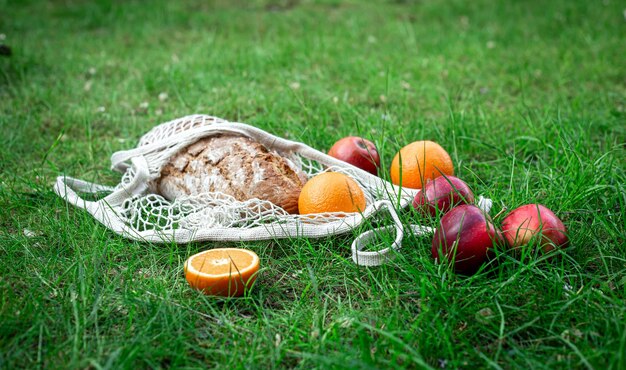 Frutas y pan fresco en una bolsa de hilo en la hierba