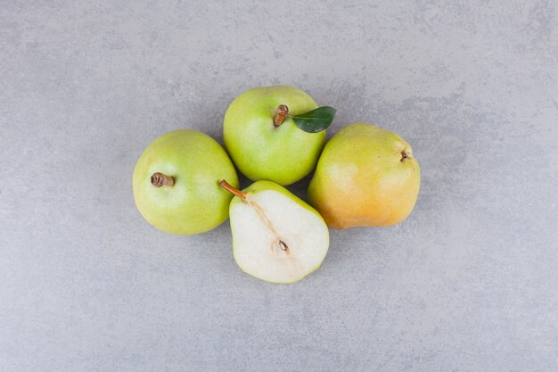 Frutas de pera enteras y en rodajas con hojas colocadas sobre una mesa oscura.