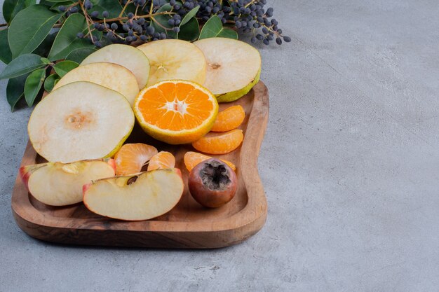 Frutas en rodajas agrupadas sobre una tabla de madera sobre fondo de mármol.