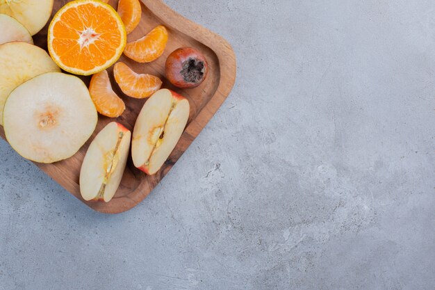 Frutas en rodajas agrupadas sobre una tabla de madera sobre fondo de mármol.