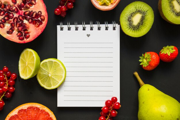 Frutas sanas jugosas con la libreta espiral en fondo negro