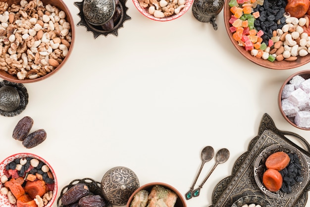 Frutas secas; nueces; fechas; Lukum y baklava en un recipiente metálico sobre fondo blanco con espacio en el centro