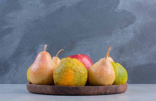 Frutas de temporada en placa de madera sobre fondo gris.