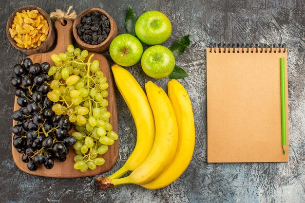 frutas uvas frutos secos plátanos tres manzanas cuaderno de crema y lápiz verde