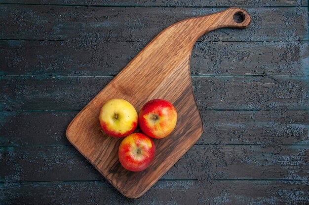 Frutas de la vista superior a bordo de tres manzanas de color amarillo rojizo sobre una tabla de cortar de madera sobre una superficie gris