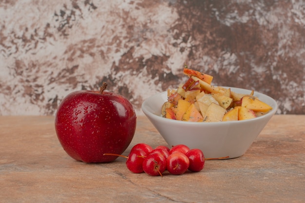 Frutero, manzanas cereza y manzana fresca sobre mesa de mármol.