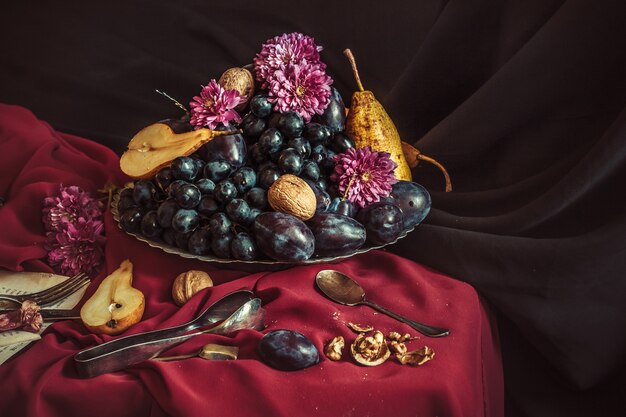 El frutero con uvas y ciruelas contra un mantel marrón