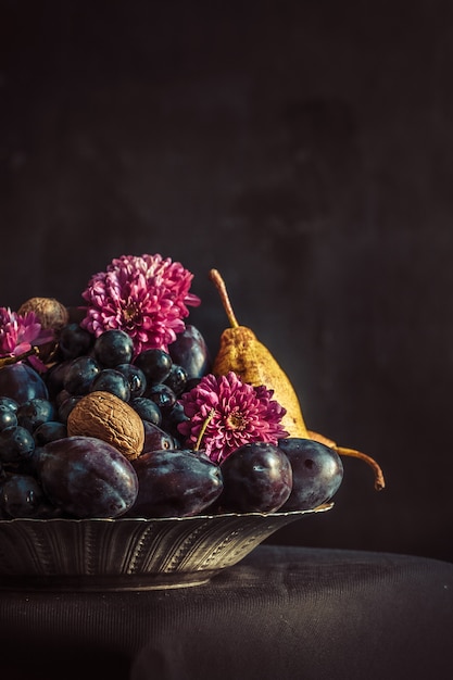 El frutero con uvas y ciruelas contra una pared oscura