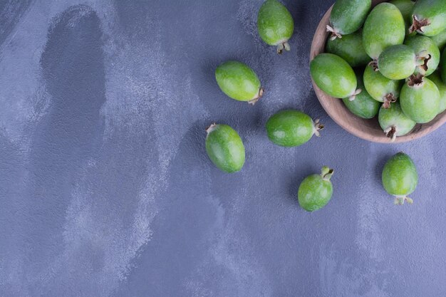 Frutos de feijoa verde en una taza de madera en el cuadro azul.