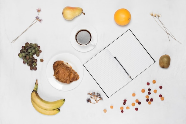 Frutos sanos; café; Croissant y pluma con cuaderno de una sola línea en blanco sobre fondo blanco