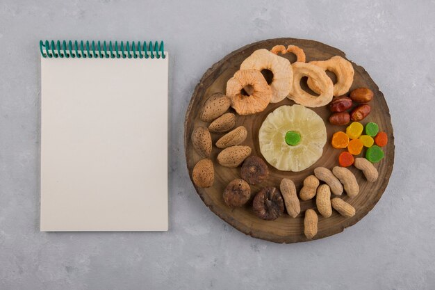 Frutos secos y bocadillos en una bandeja de madera con un cuaderno a un lado