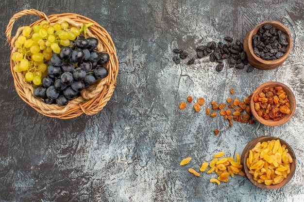 Foto gratuita frutos secos canasta de madera de uvas verdes y negras y frutos secos en tazones