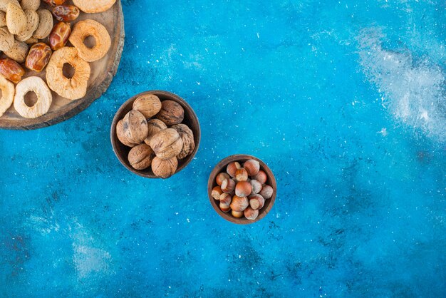 Frutos secos y nueces sabrosas en un tablero, sobre la mesa azul.