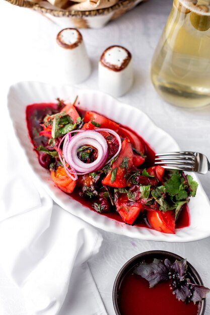Una fuente de ensalada de tomate con cebolla roja hojas oscuras albahaca cilantro eneldo