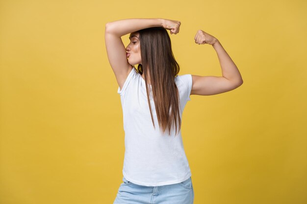 Fuerte y energía Bastante joven morena mostrando bíceps en su brazo Colorido retrato de estudio con fondo amarillo