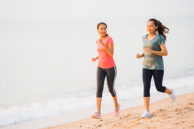 Funcionamiento y ejercicio asiáticos de la mujer del deporte joven hermoso del retrato en la playa cerca del mar y del océano en el tiempo de la salida del sol o de la puesta del sol