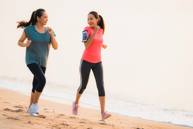 Funcionamiento y ejercicio asiáticos de la mujer del deporte joven hermoso del retrato en la playa cerca del mar y del océano en el tiempo de la salida del sol o de la puesta del sol